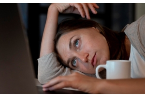 Frau lümmelt müde vor dem Laptop wegen Problemen mit der Leber