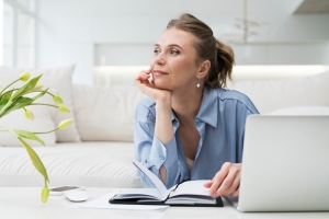 Frau schaut bei der Arbeit am Laptop in die Luft und sollte ihre Konzentration verbessern